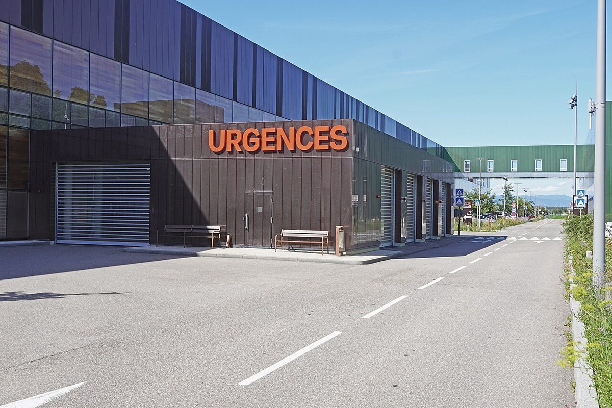 Enseigne orange « URGENCES » sur la façade d’un hôpital, au bord d’une route vide